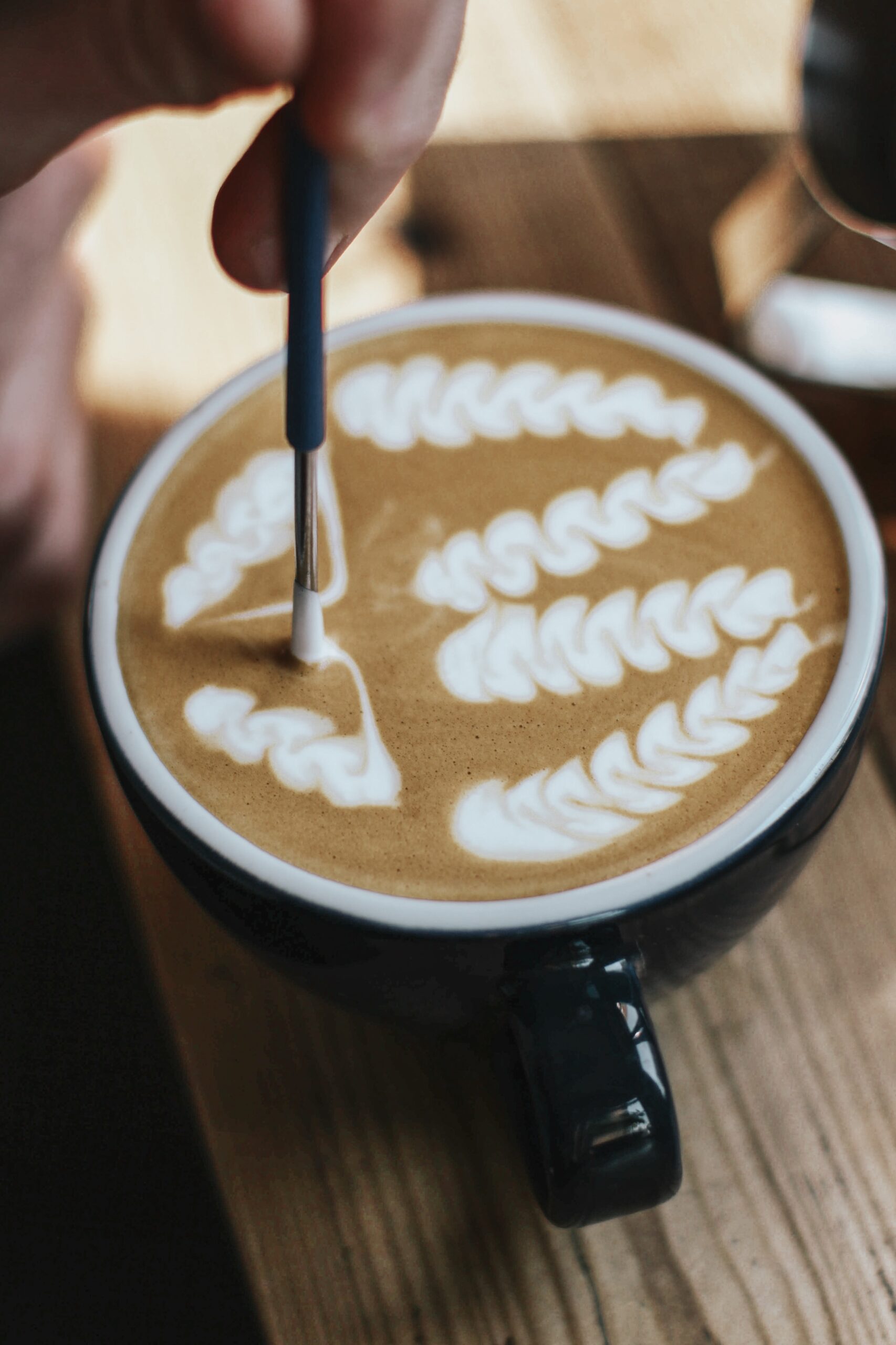 A selective closeup shot of coffee with latte art in a black ceramic cup on a wooden surface